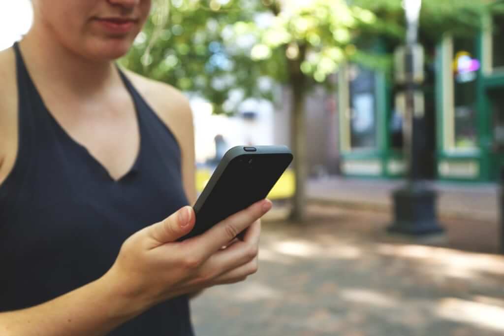 Woman looking at her phone on the street with trees in background