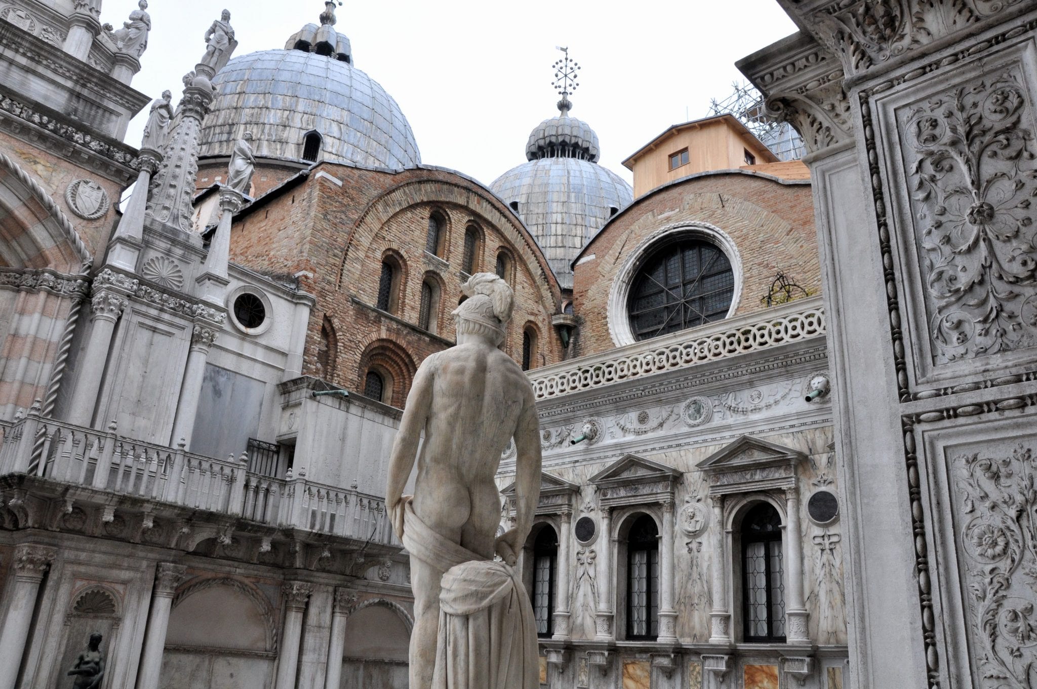 Marble statue in the courtyard of the Doge’s Palace in Venice, with domes and ornate Gothic architecture in the background.
