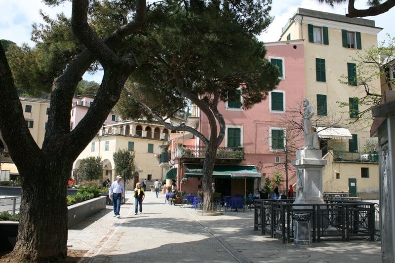 One of the Cinque Terre off season towns, with a couple of tourists walking along a promenade with a statue and trees, in front of pink and white houses.