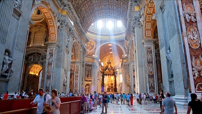 The interior of St Peter´s Basilica with rays of sunlight streaming through the windows of the majestic dome onto the people who are visiting below