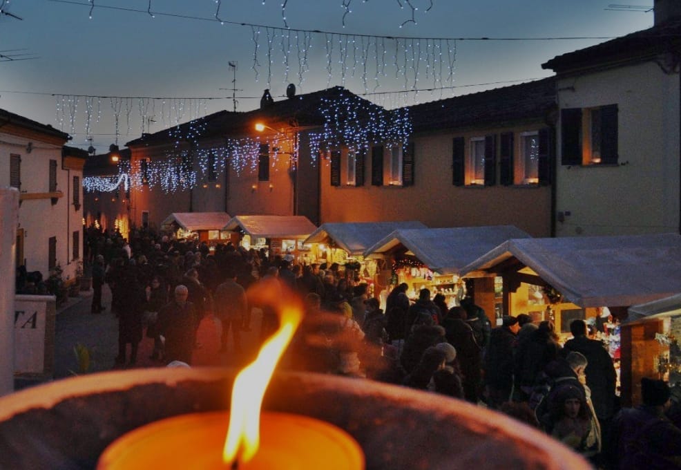 The Candelara Christmas Market in Italy, a close up of the candle with the candlelit market stalls in the background, in front of Italian houses in the town