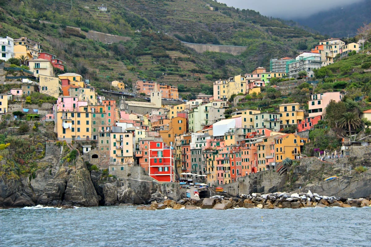 Several colorful buildings rising up through the rugged landscape in front of the ocean.
