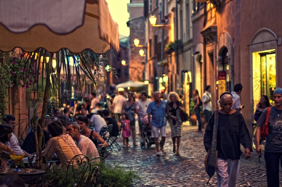 Groups of people walking on cobbled street at dusk in Trastevere in Rome.
