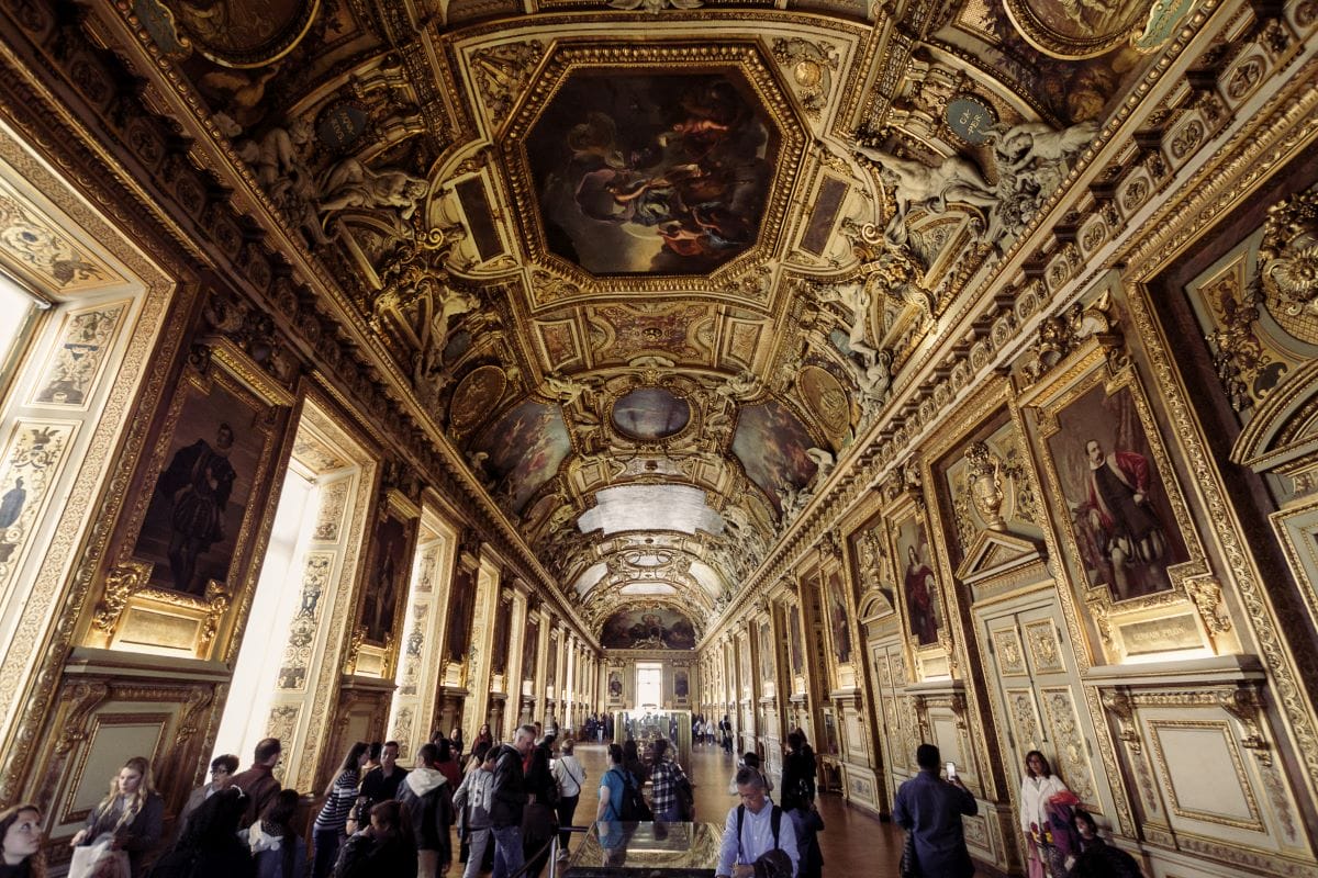 Visitors taking in the spectacular rooms while touring the famous Louvre Museum.