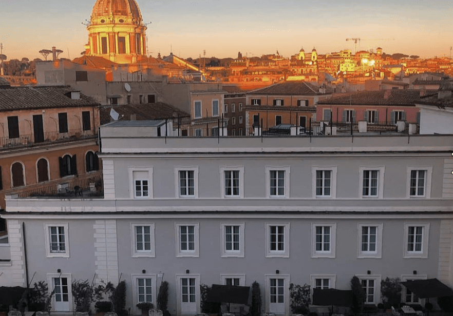 A view of a row of apartments in a modenr grey and white block, in front of terracotta roofs and the duomo of the old town in the distance.