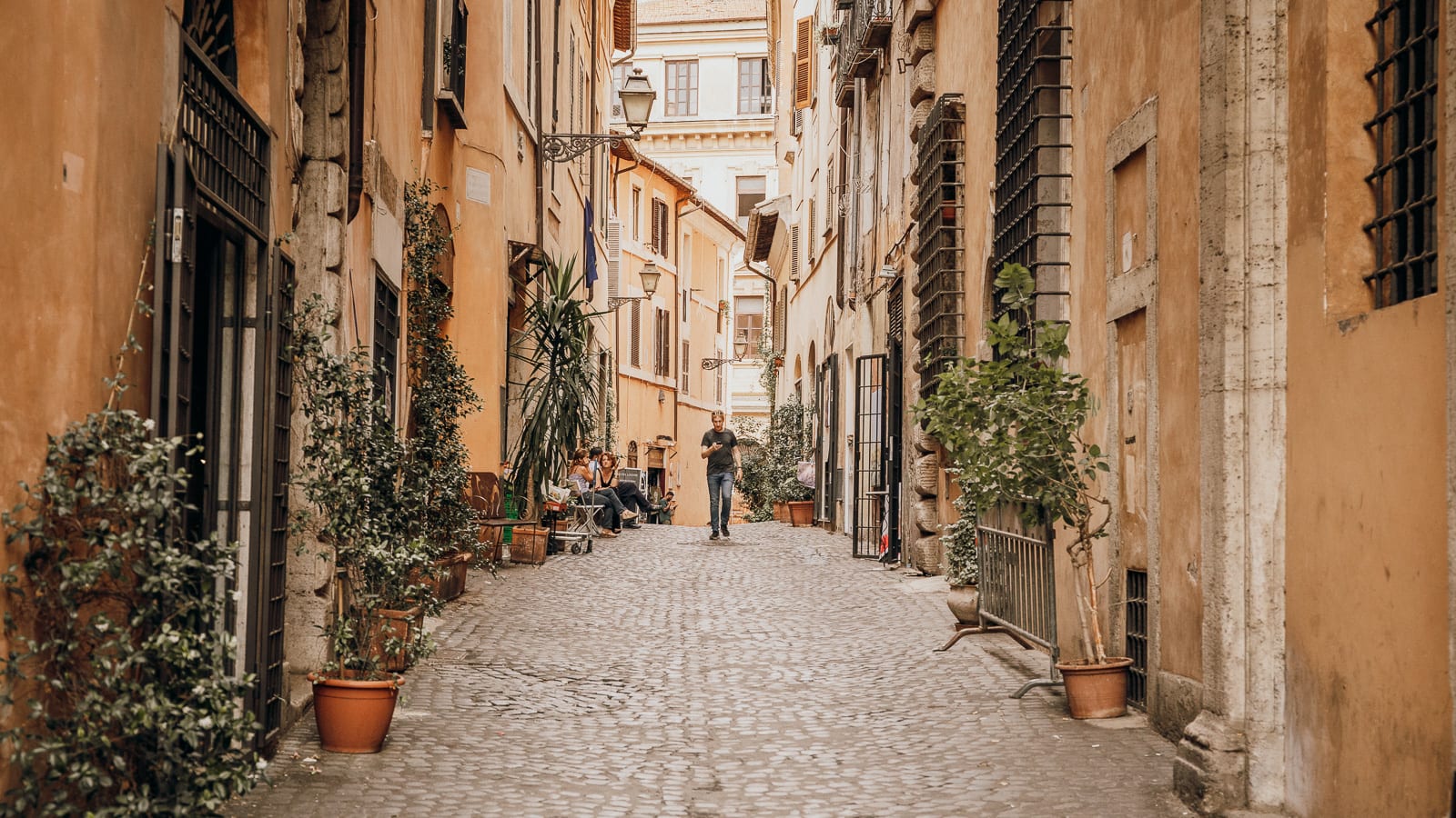 A man walking through a quiet street in Rome's Trastevere neighborhood.