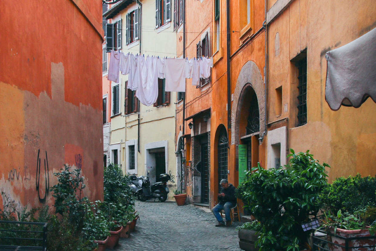 Man sitting on a doorstep with laundry above his head in a quiet Roman neighborhood