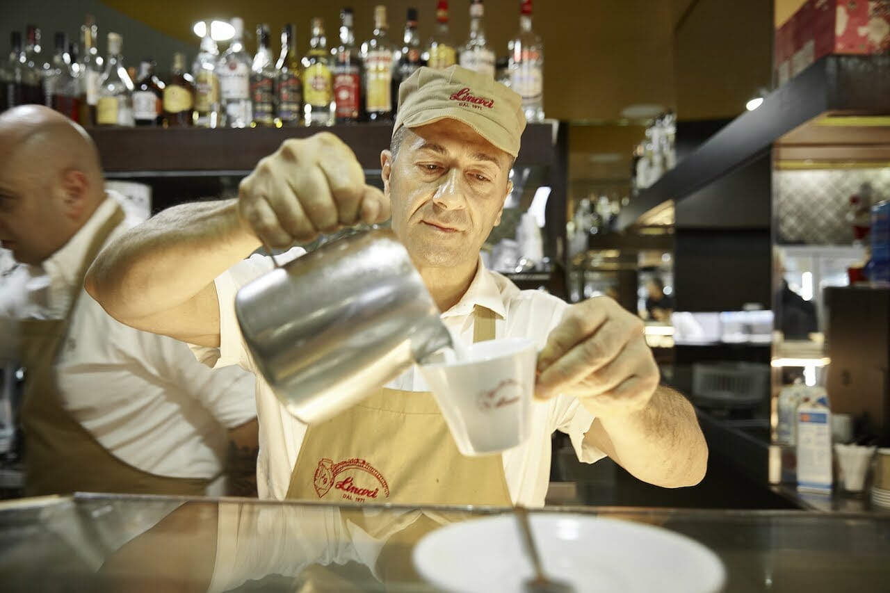 Barman pours heated milk into a tiny coffee or espresso cup in Rome.