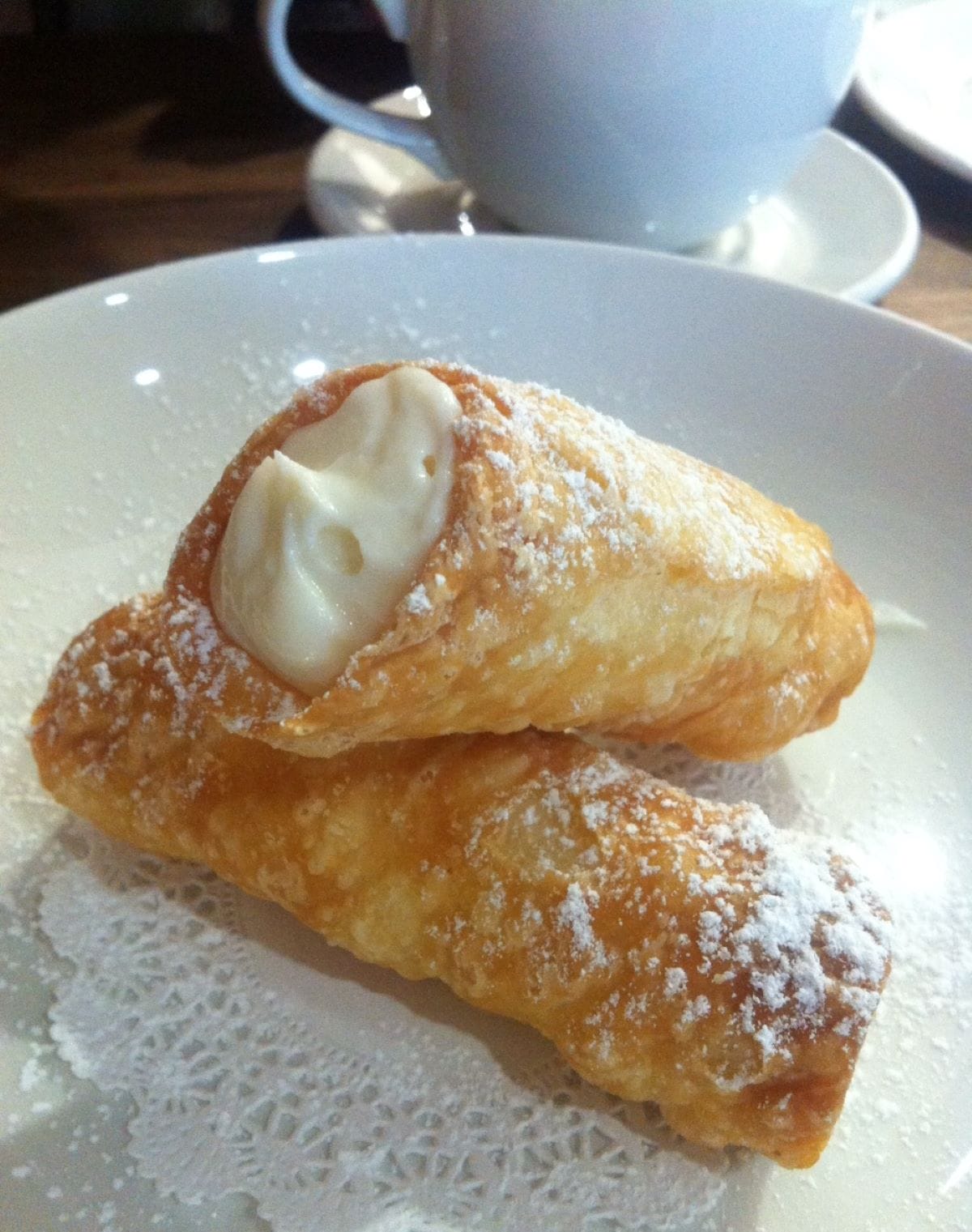 closeup of two cannolis with coffee in the background. 
