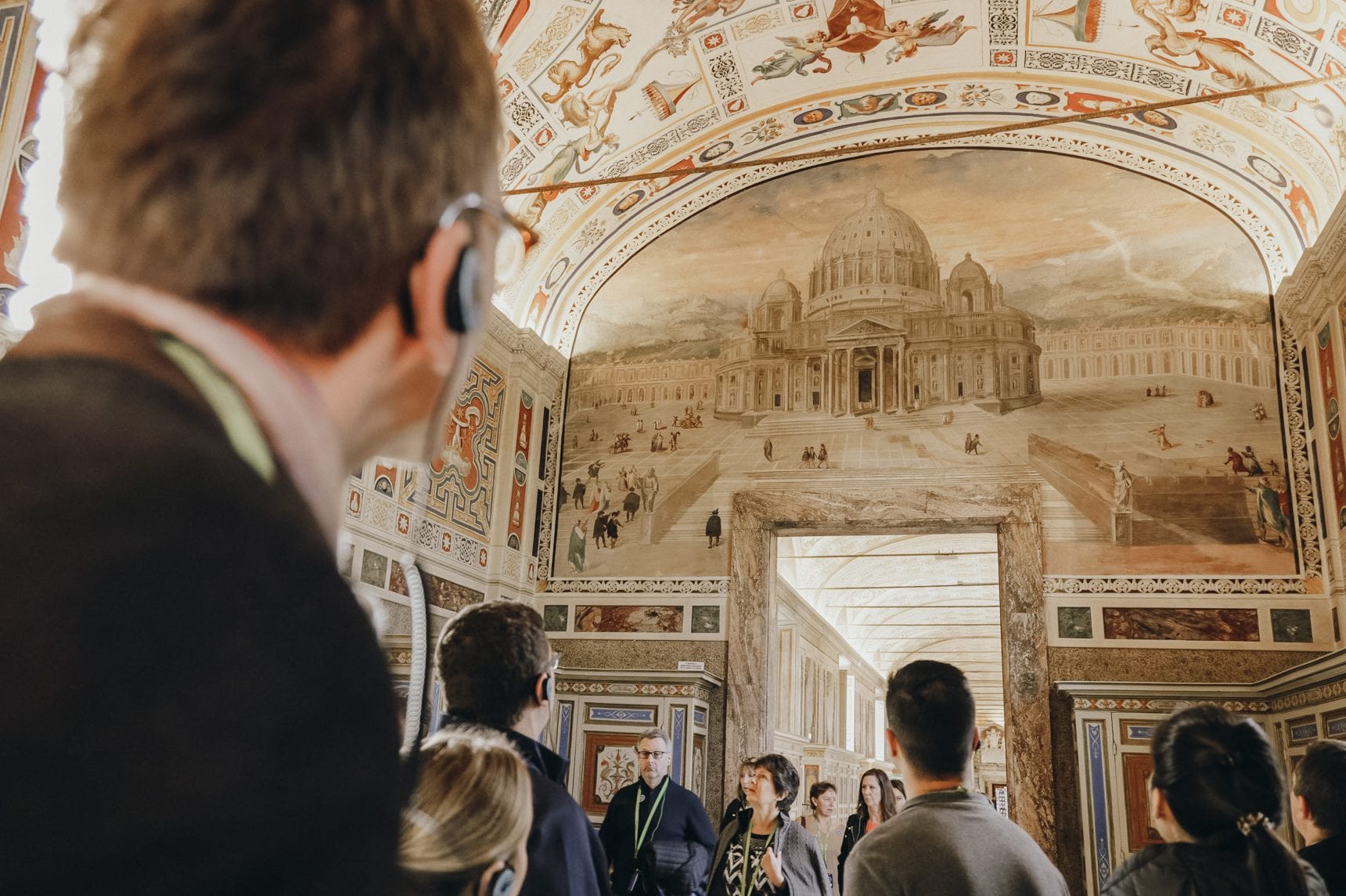 A tour group with a guide, stand in awe, looking at the ornate painted walls of one of the rooms you visit on the Vatican Tour