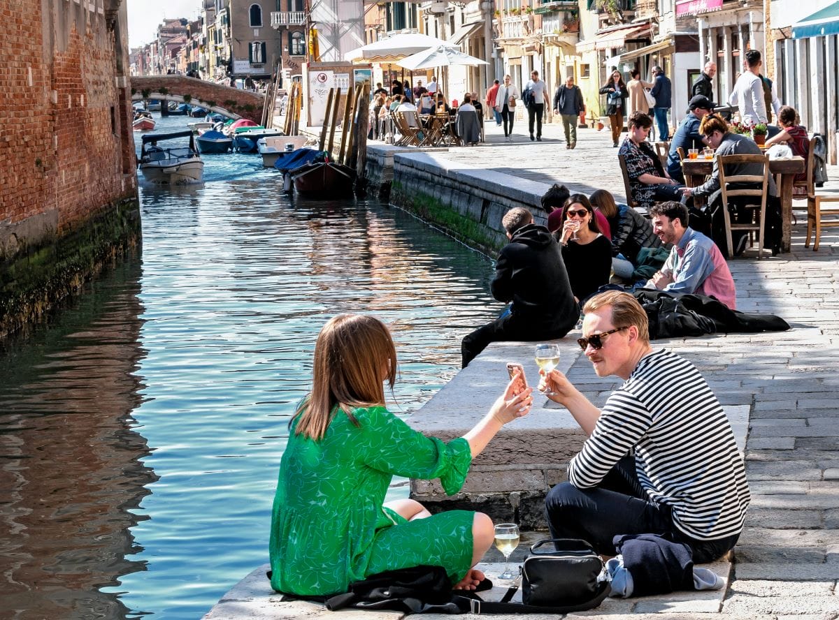 People sitting by the canals in Venice enjoying drinks. 