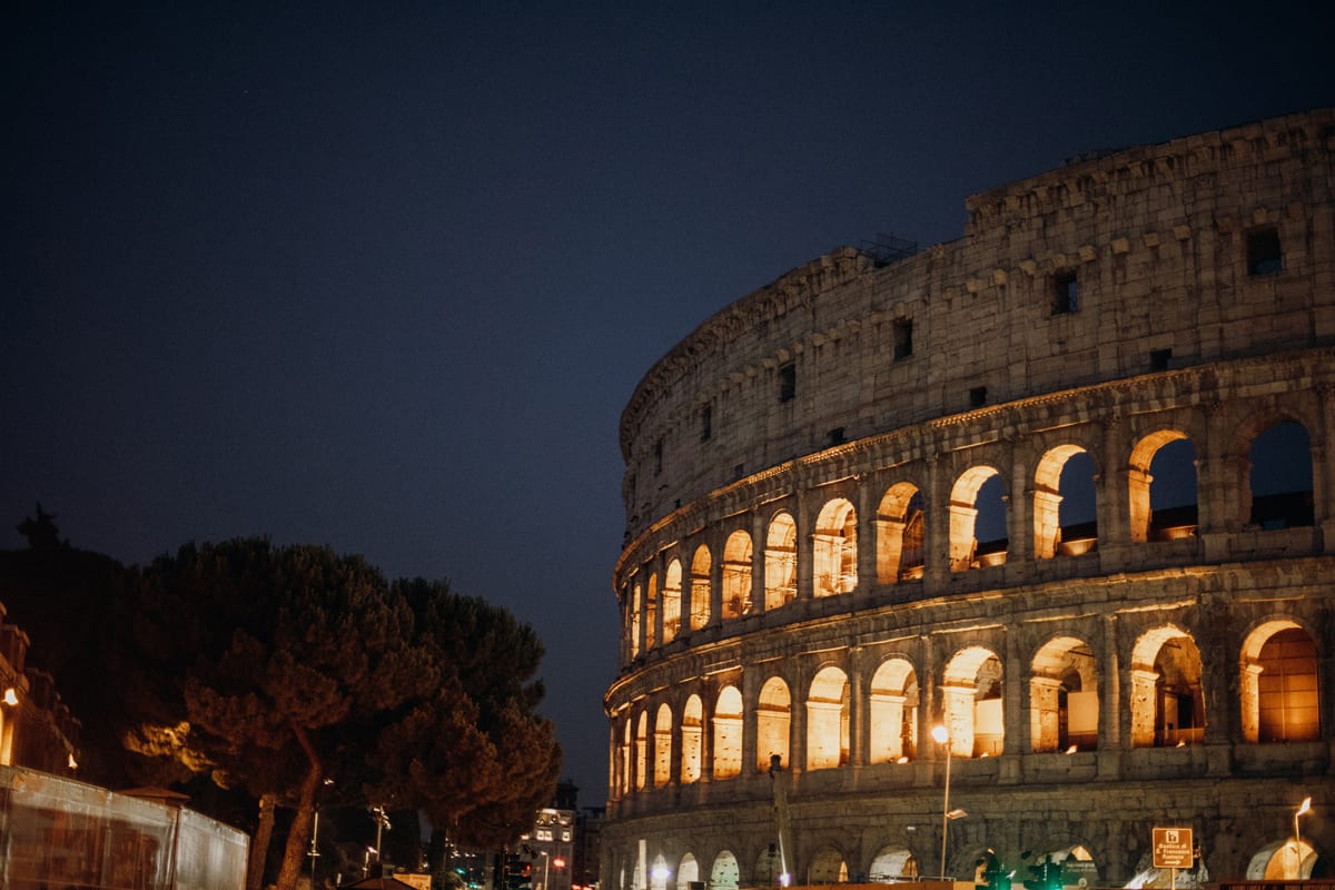 The Colosseum at Night, with light glowing through the famous arches on each level. Hear more about this architectural wonder with podcasts on Ancient Rome 