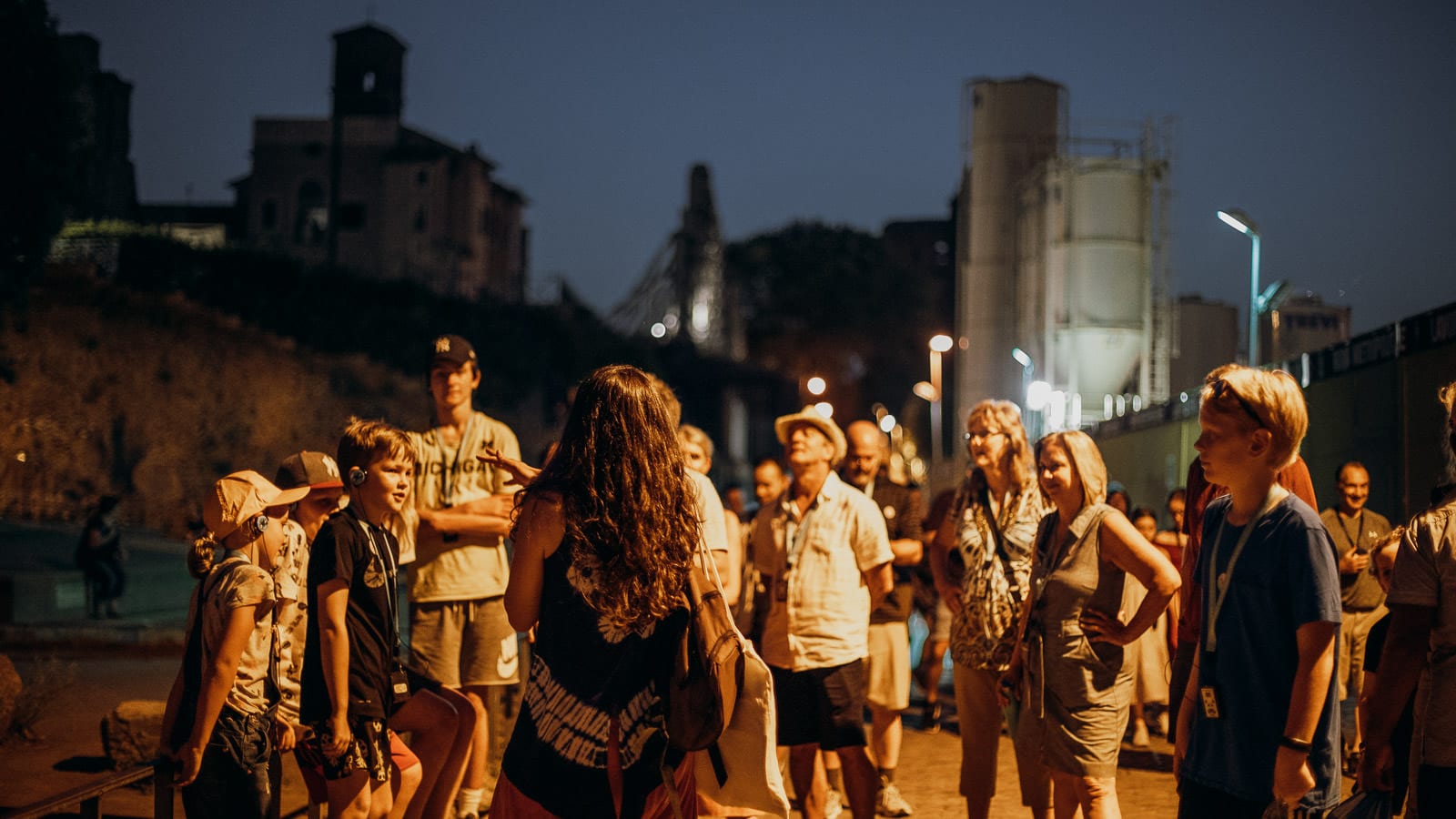 a nighttime view of a group of tourists with a tour guide, in the city of Rome with the silhouette of buildings in the background