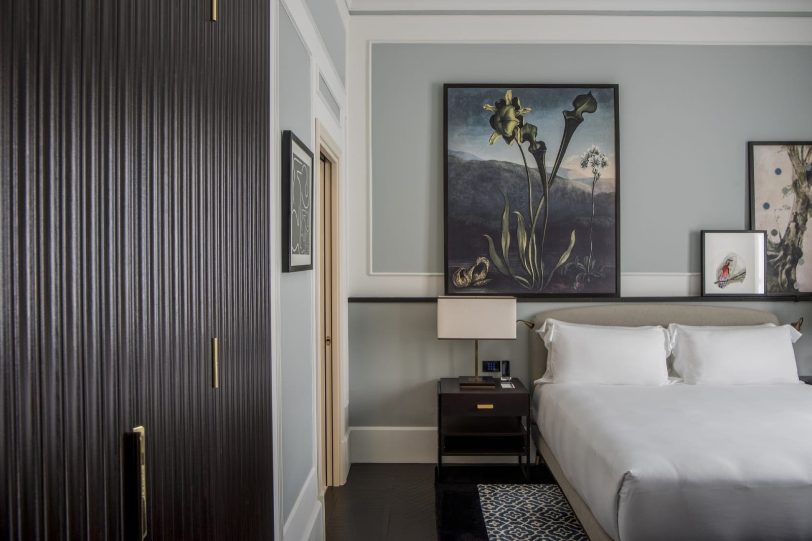 a hotel room with double bed and bedside cabinet, and modern style decor including a variety of paintings above the headboard.