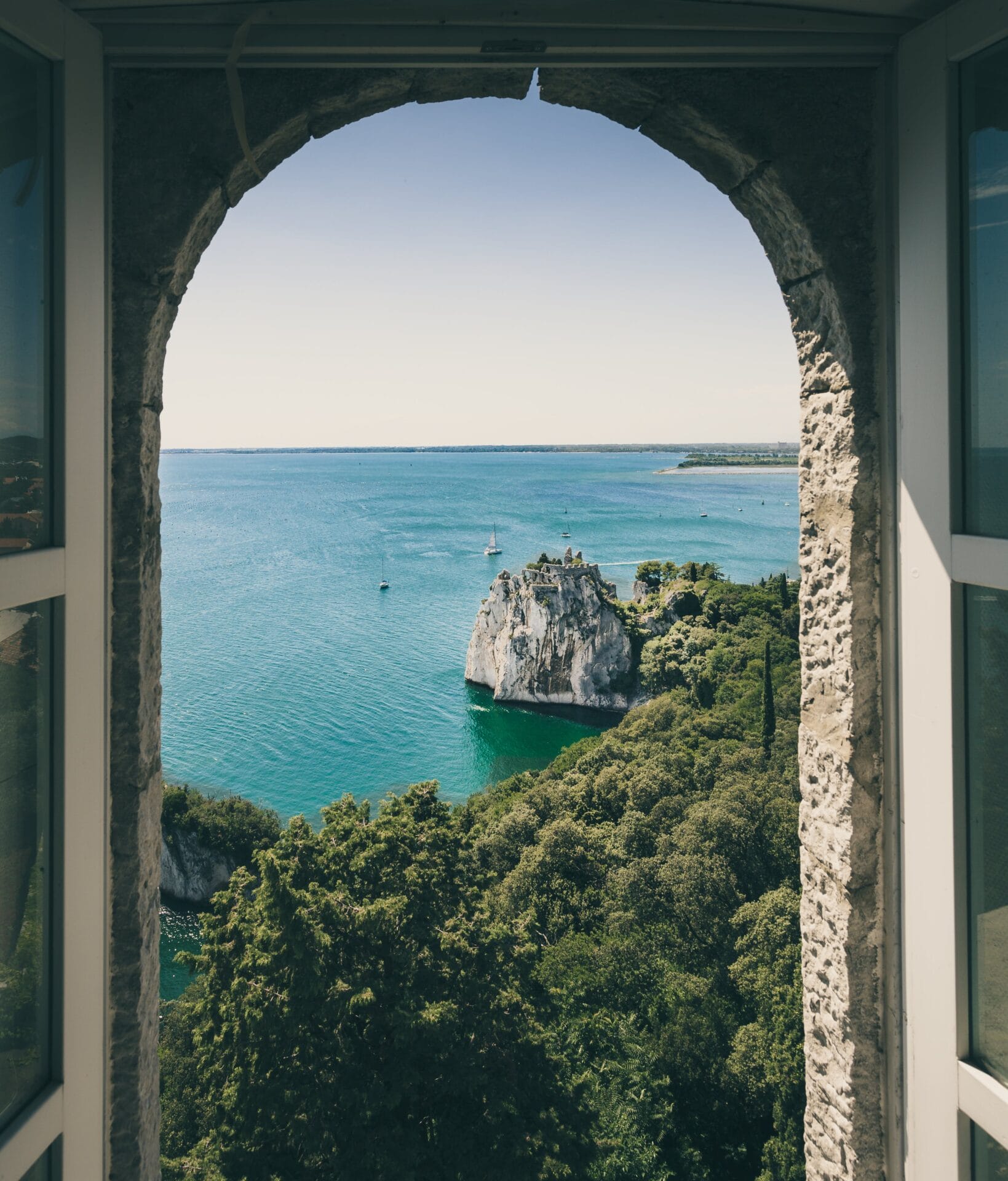 Duino window with forest and body of water blue sky