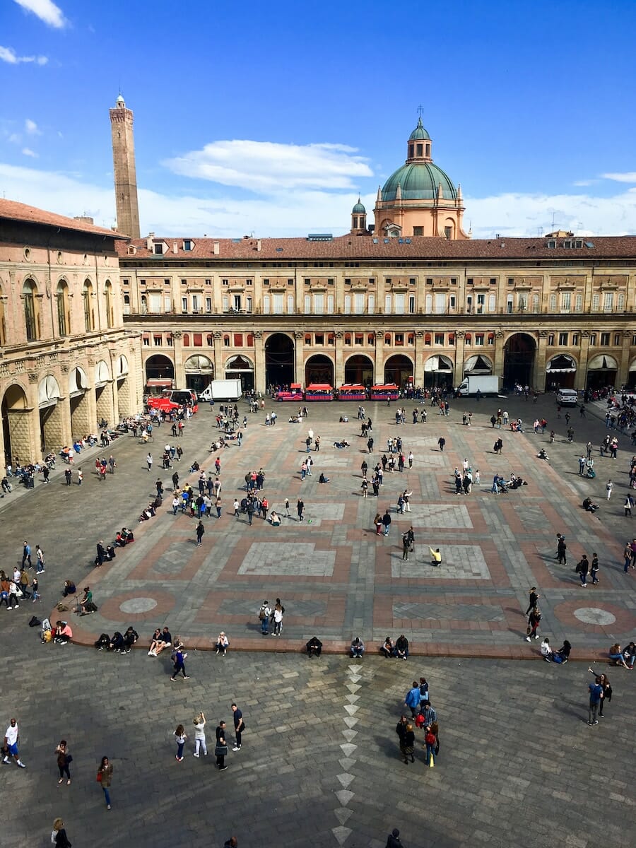 people walking near Bologna's Piazza Maggiore under blue and white skies
