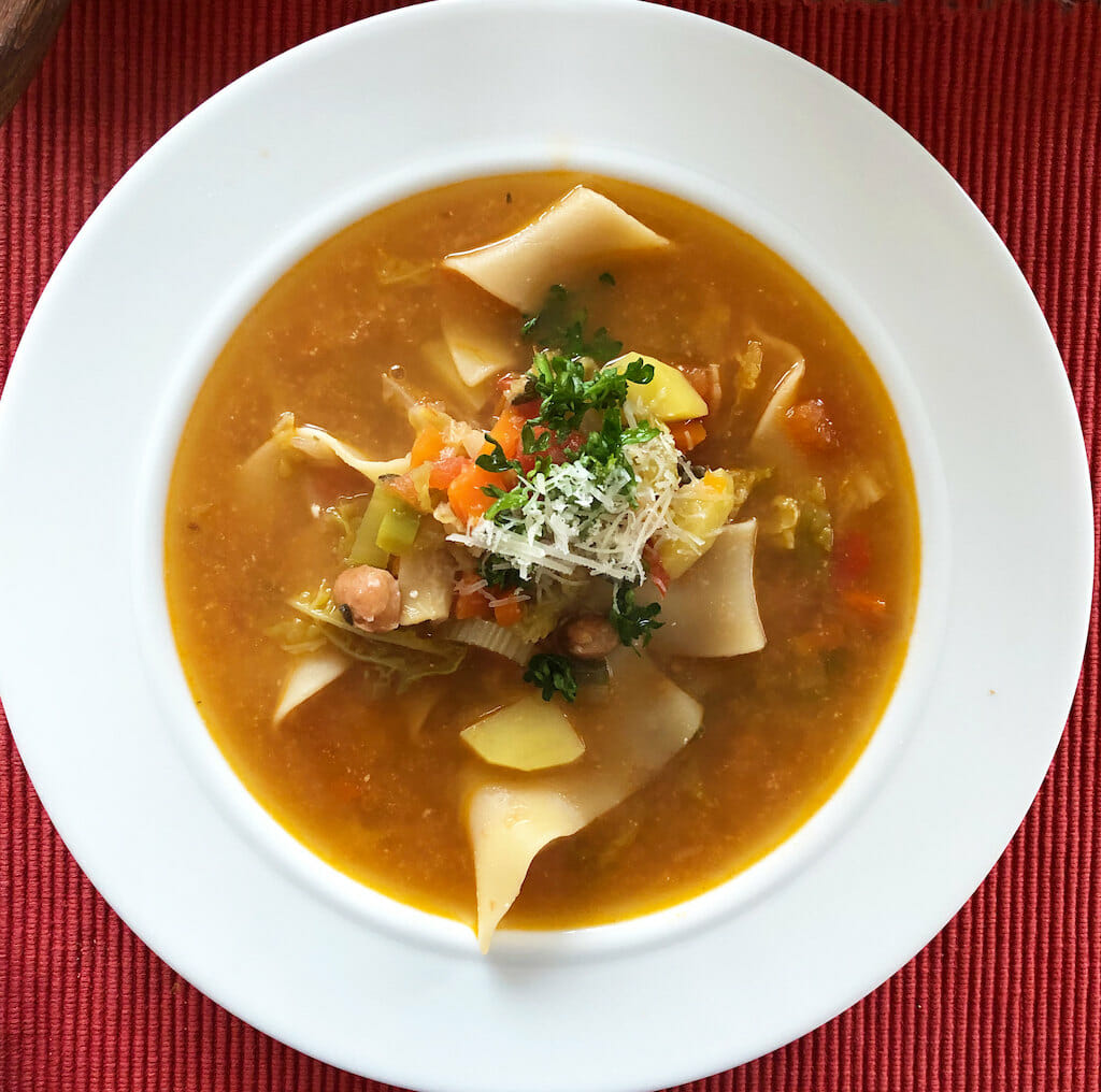 Soup plate filled with risotto milanese with beans, pasta, celery, and other vegetables.