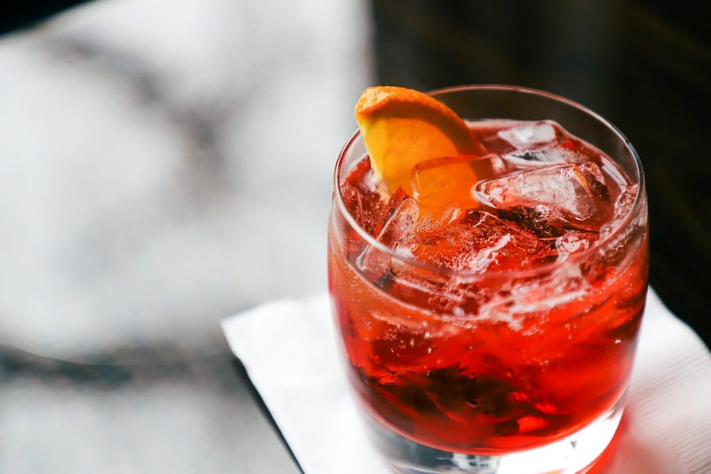 Red, fizzy cocktail in a glass with ice cubes and an orange slice on a napkin