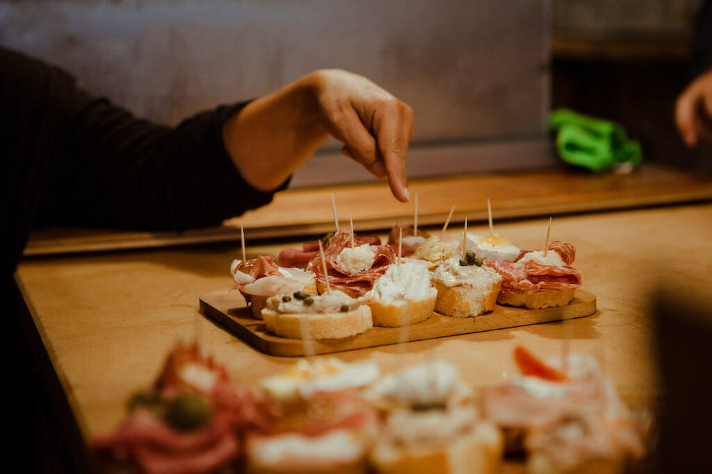 Hand pointing to different type of cicchetti on top of bread in Venice with toothpicks