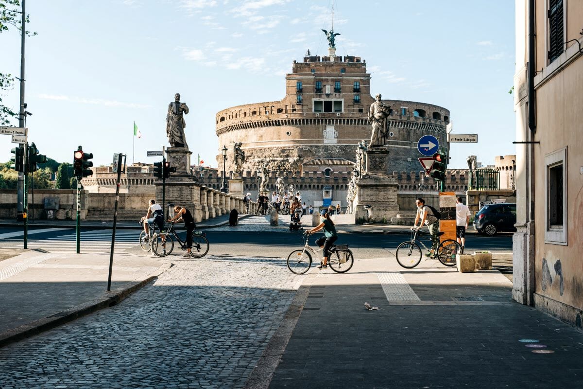People riding bikes on the street of Rome with a castle in the background