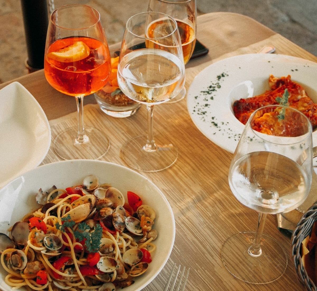 Plates of seafood pasta surrounding by glasses of wine and Aperol Spritz