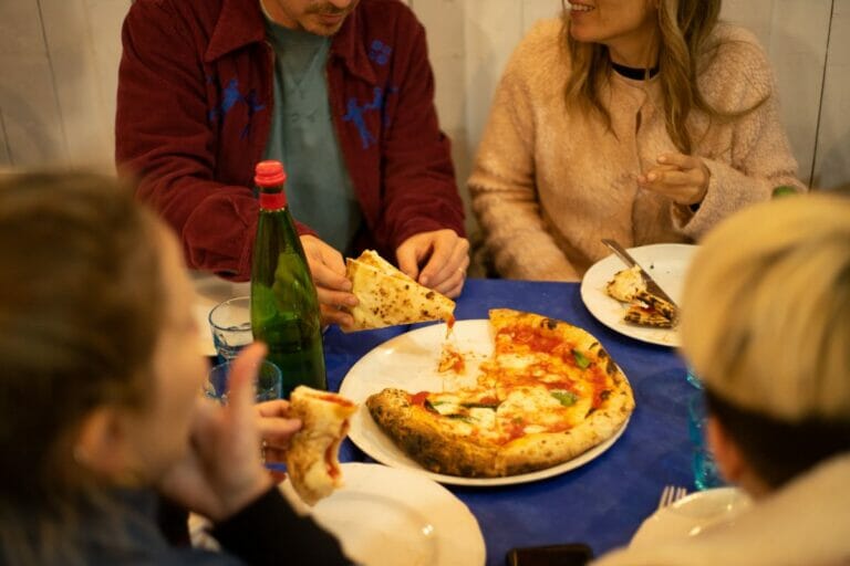People sit at a table and eat pizza, one of the most iconic foods to eat in Italy