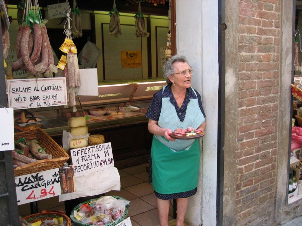 a shop owner holding a tray of meats and cheeses for guests to try
