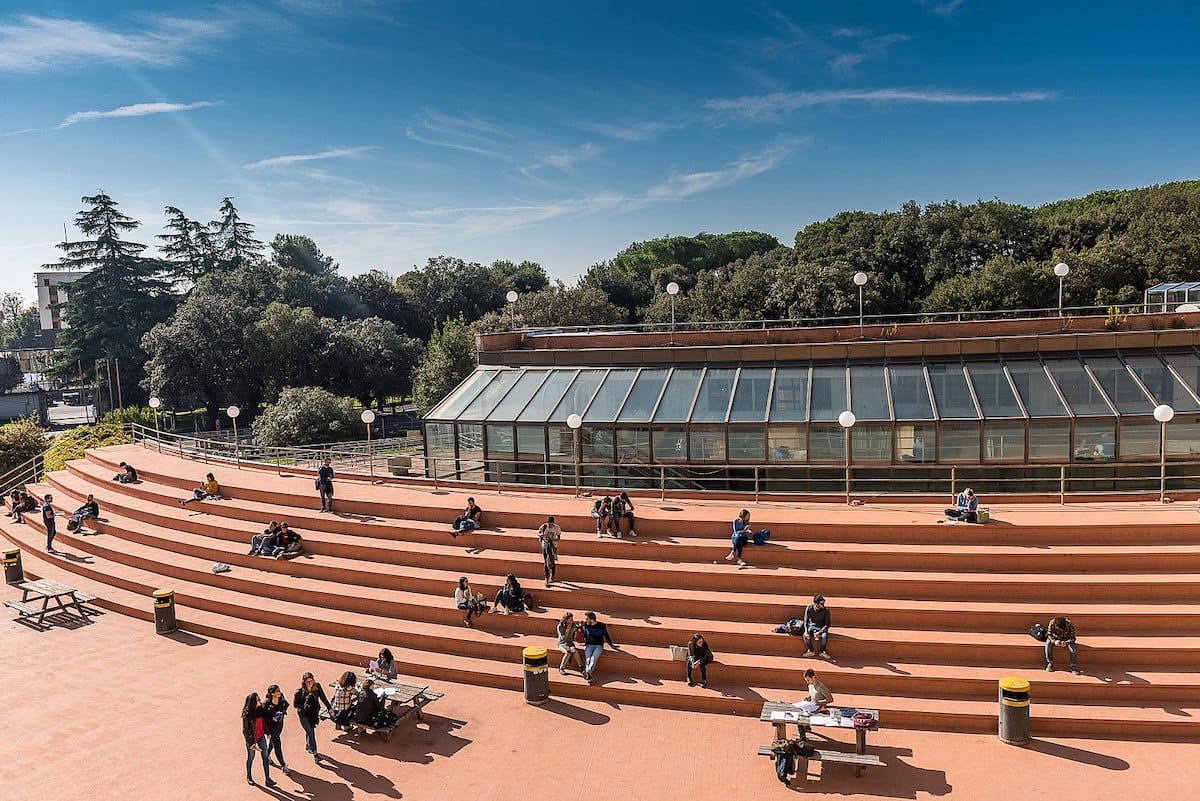 students sitting on steps outside a university on a sunny day