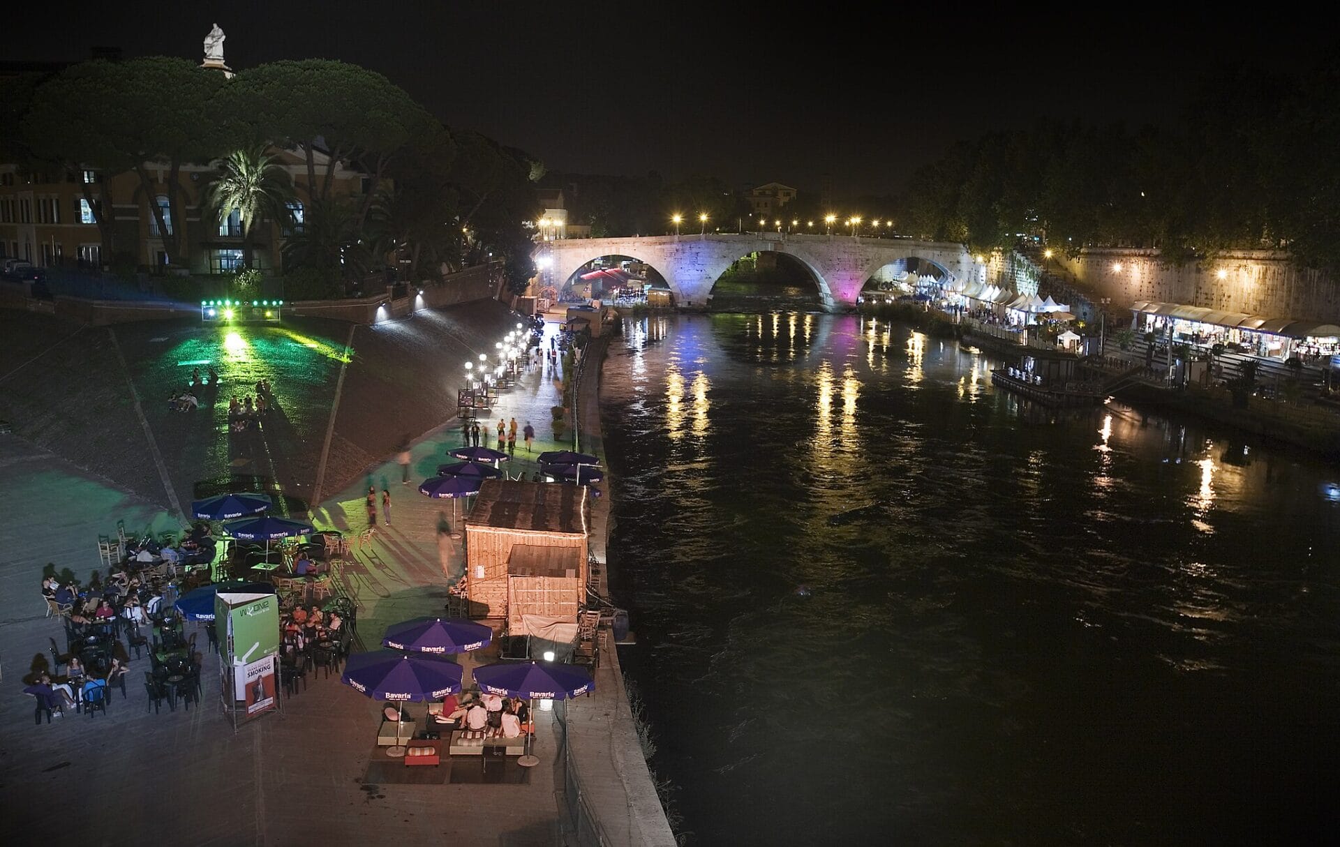 Several people enjoying an event at Rome's Tiber Island (Isola del Cinema) at night.