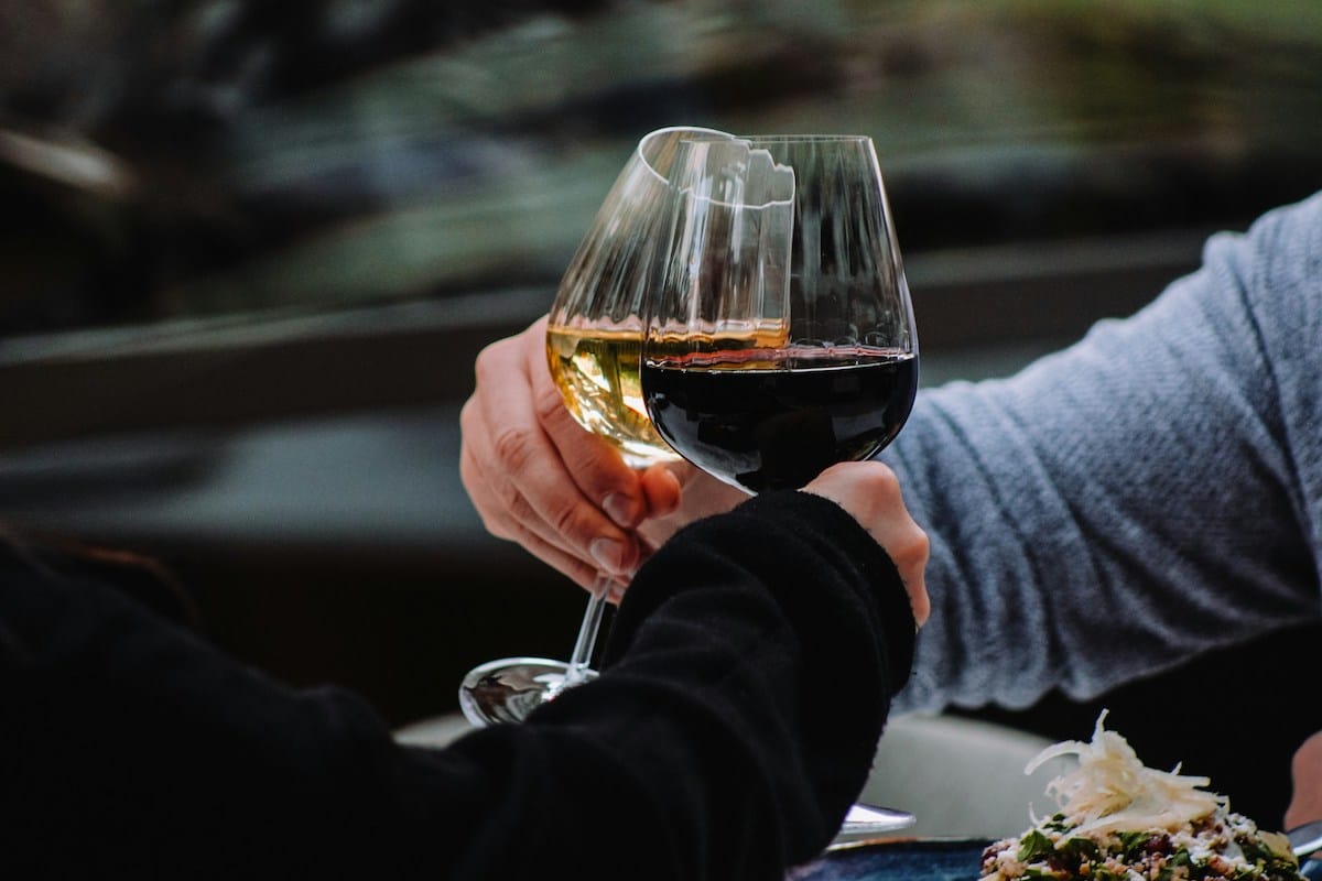 Two people toasting with a glass of red wine and a glass of white wine.