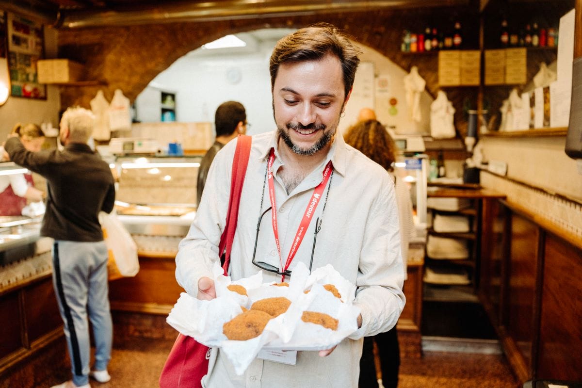 A bearded man happily looking down at a tray of supplì in Rome, Italy.