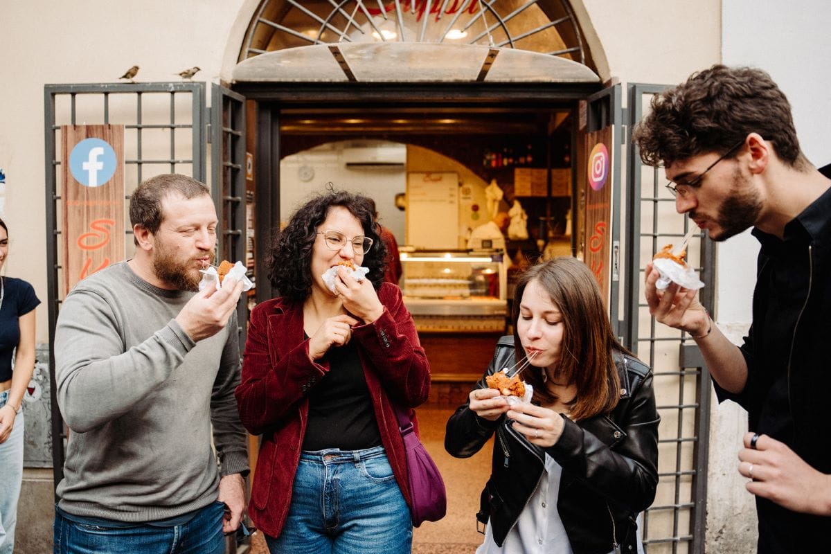 A group of people eating rice balls outside of a restaurant while on a food tour in Rome.