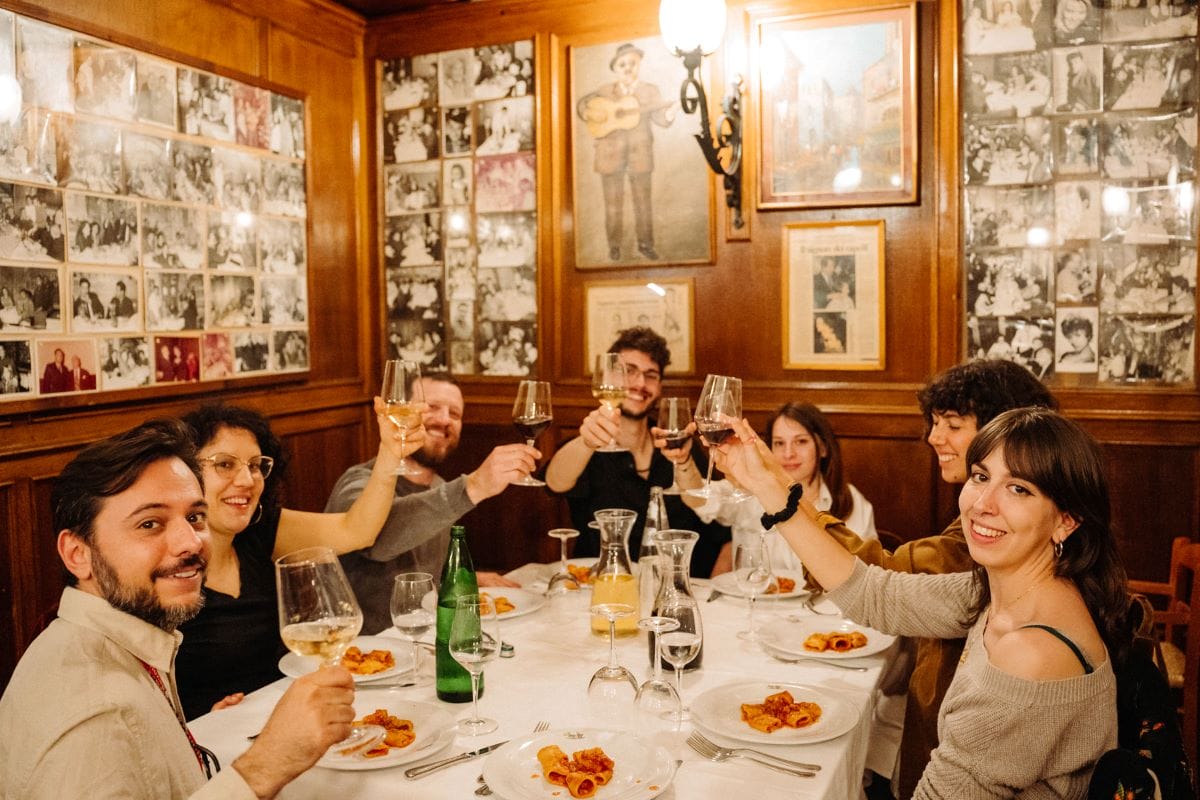 A group of people at a table smiling while cheering wine glasses while on a tour of Rome.