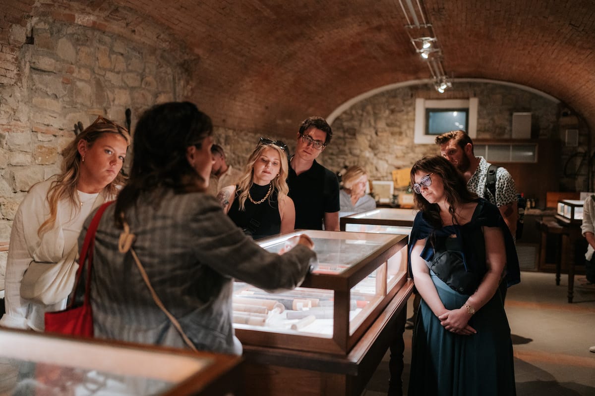 A tour guide explains some antiques in a cellar while a group looks on.