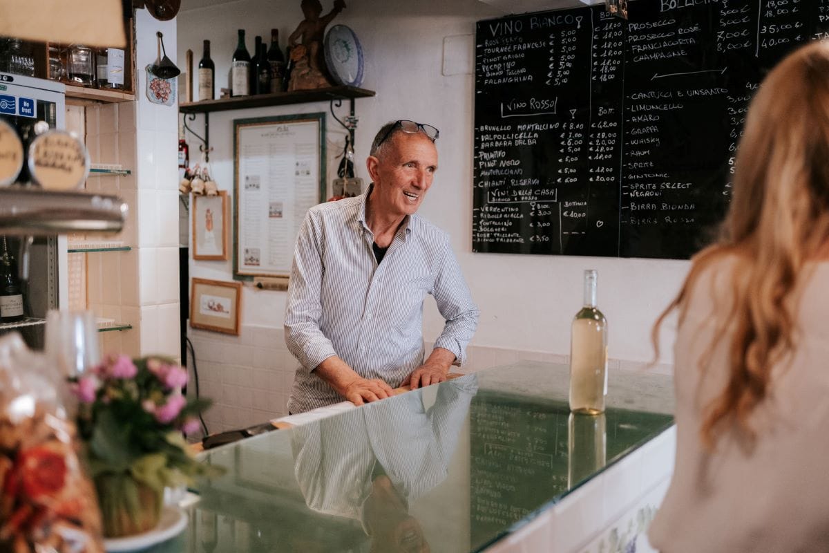 A man smiling next to a bottle of white wine on a glass bar.