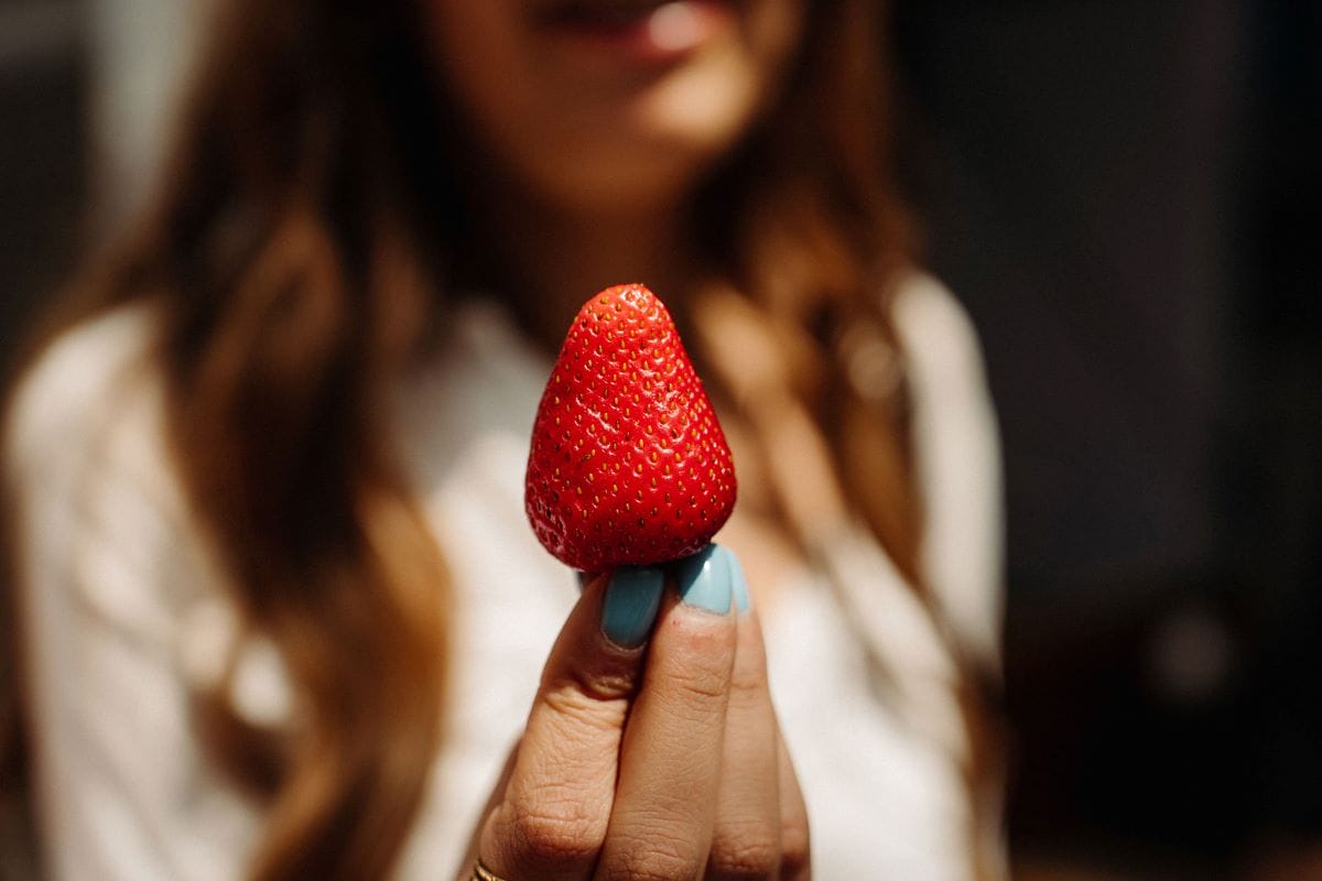 A woman with light blue fingernails holding a strawberry.