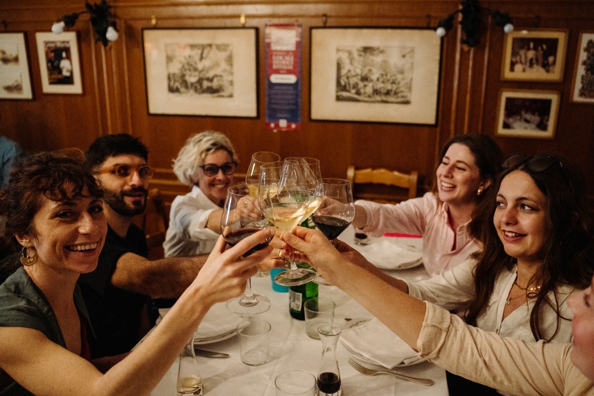 Various people at a table smiling as they toast with wine glasses in a restaurant.