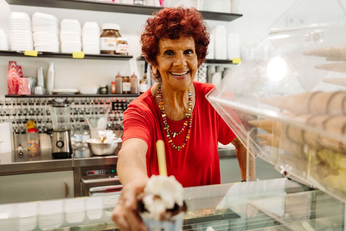 A smiling woman in red shirt serving a cup of Italian gelato.
