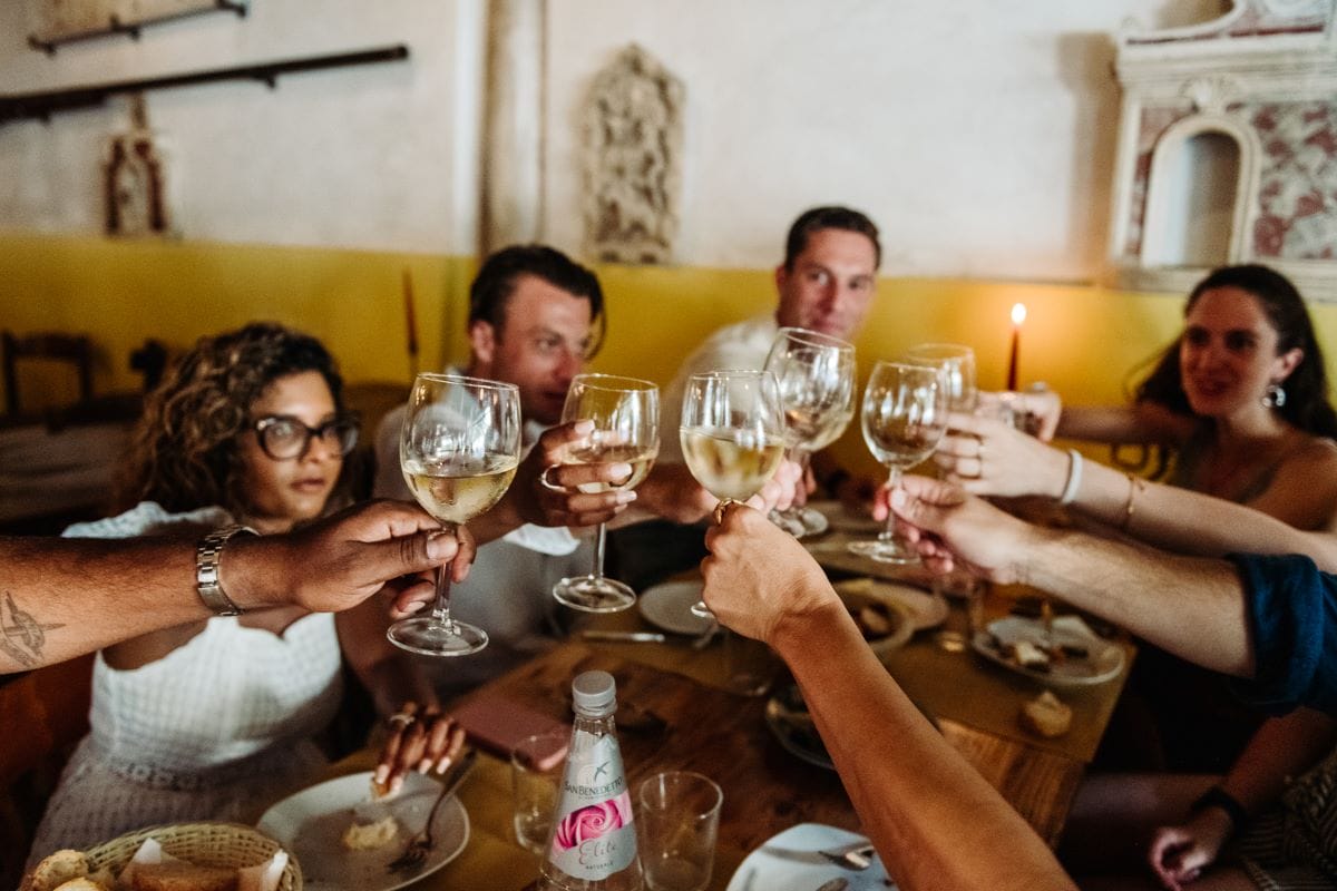 A group of people sitting at a table toasting with wine glasses.