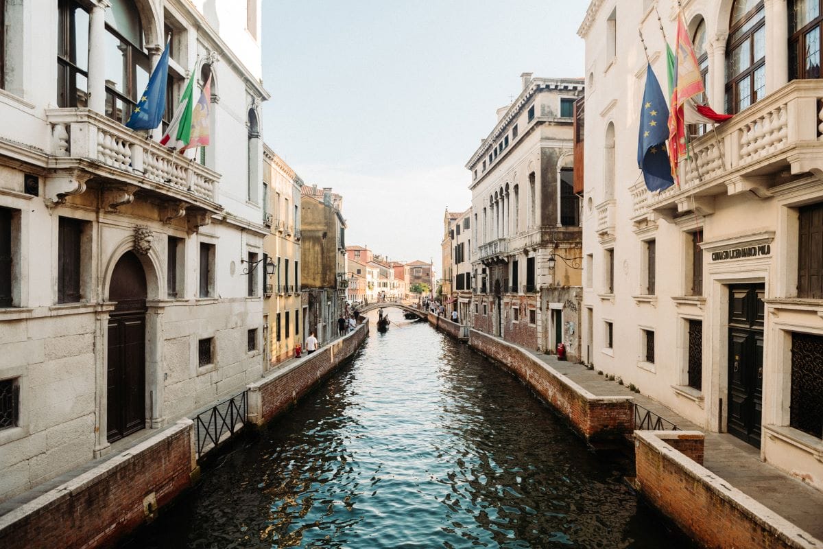 A long canal with buildings on other side and a bridge spanning over the water.