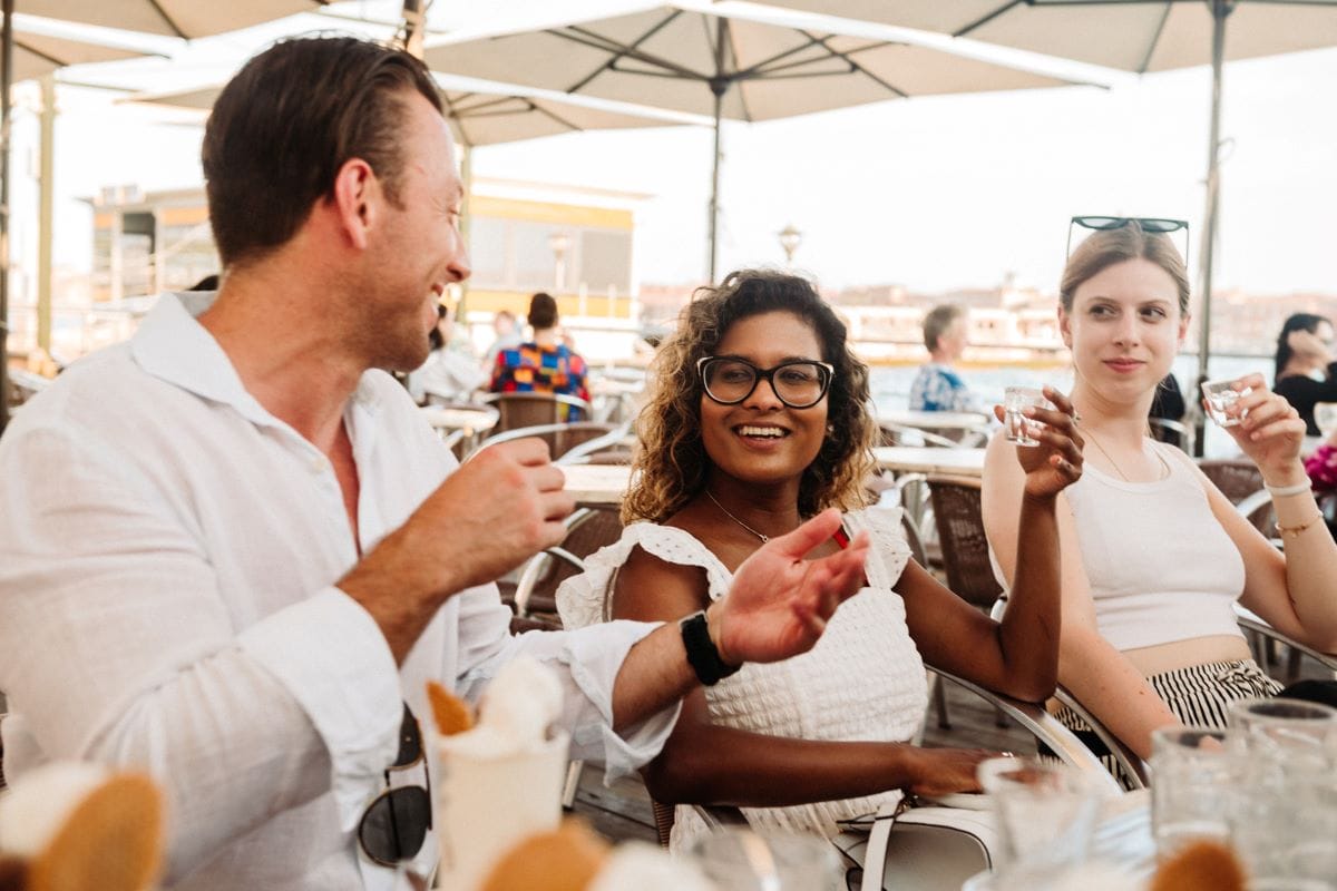 One man and two women toasting at an outdoor table in Venice.