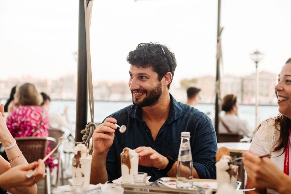 A man sitting at table smiling as he's about to try what's on his fork.