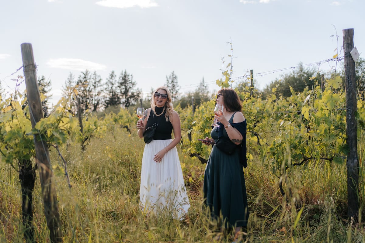 Two women laughing while drinking wine in a vineyard in Tuscany.
