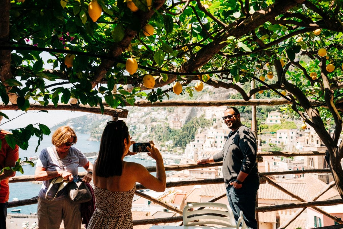 A group of people posing for a picture under a lemon tree while touring the Amalfi Coast.