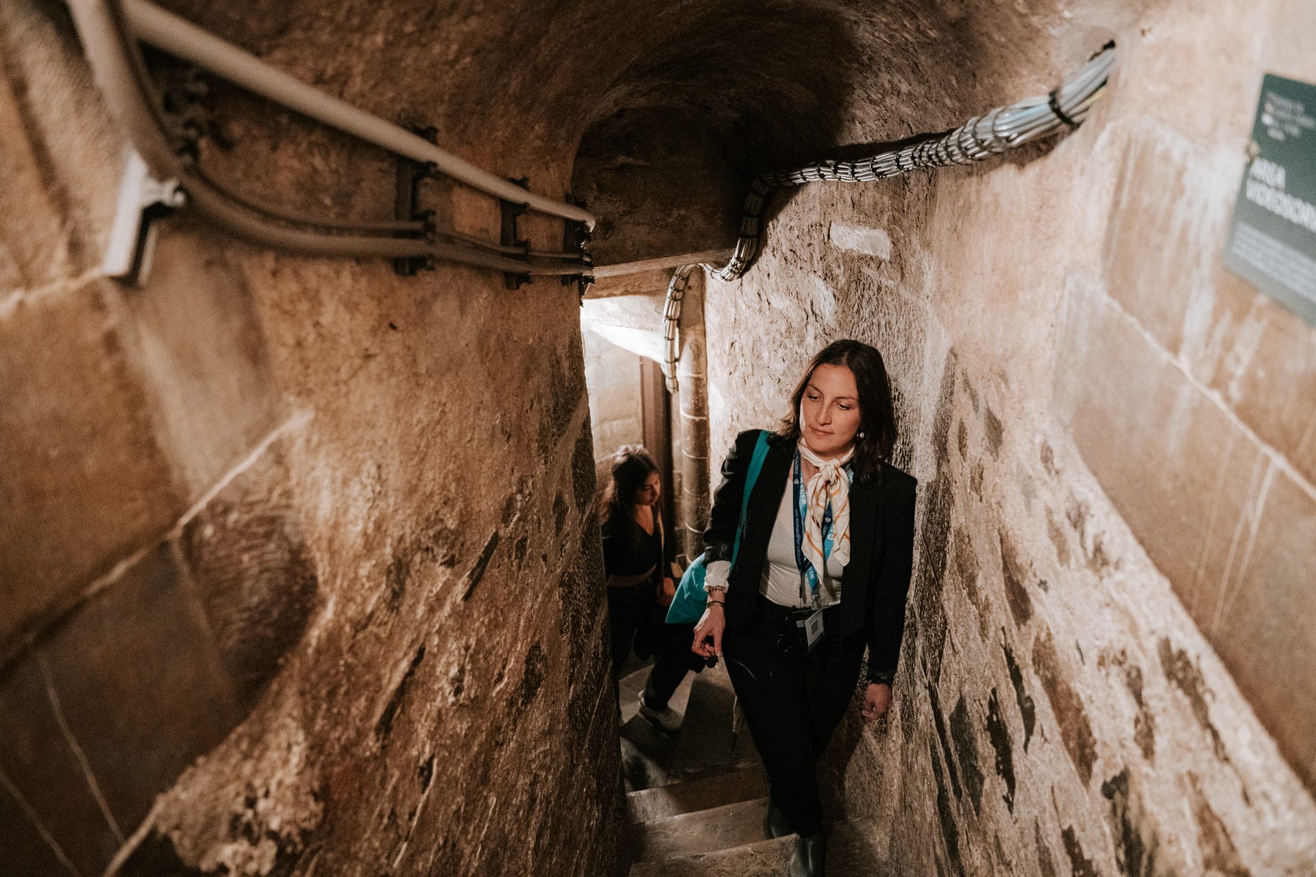 Tourists walking up narrow stone stairs inside Florence's Duomo, surrounded by ancient stone walls.