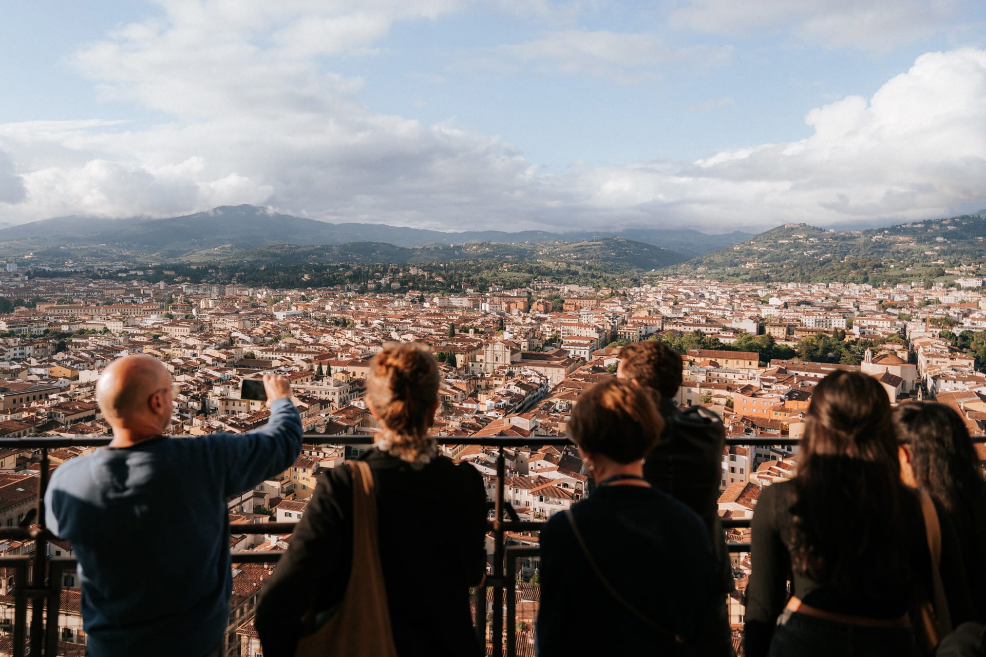 Tourists enjoying a panoramic view of Florence from the top of the Duomo, with the Tuscan hills in the distance