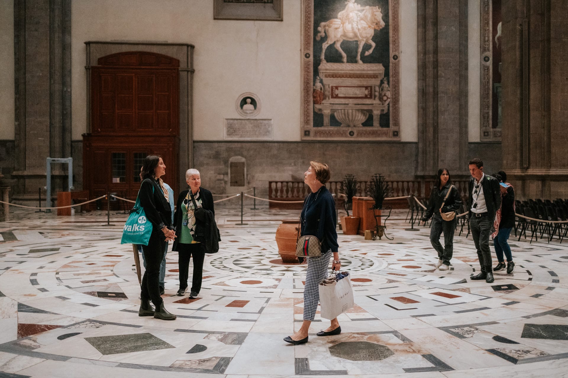 A tour group inside the Florence Cathedral, with a guide speaking to visitors on the marble floor while others explore the space.