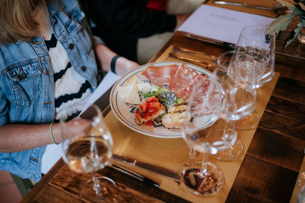 Woman sitting in front of table with a plate of various slices of ham and cheese in Tuscany. 
