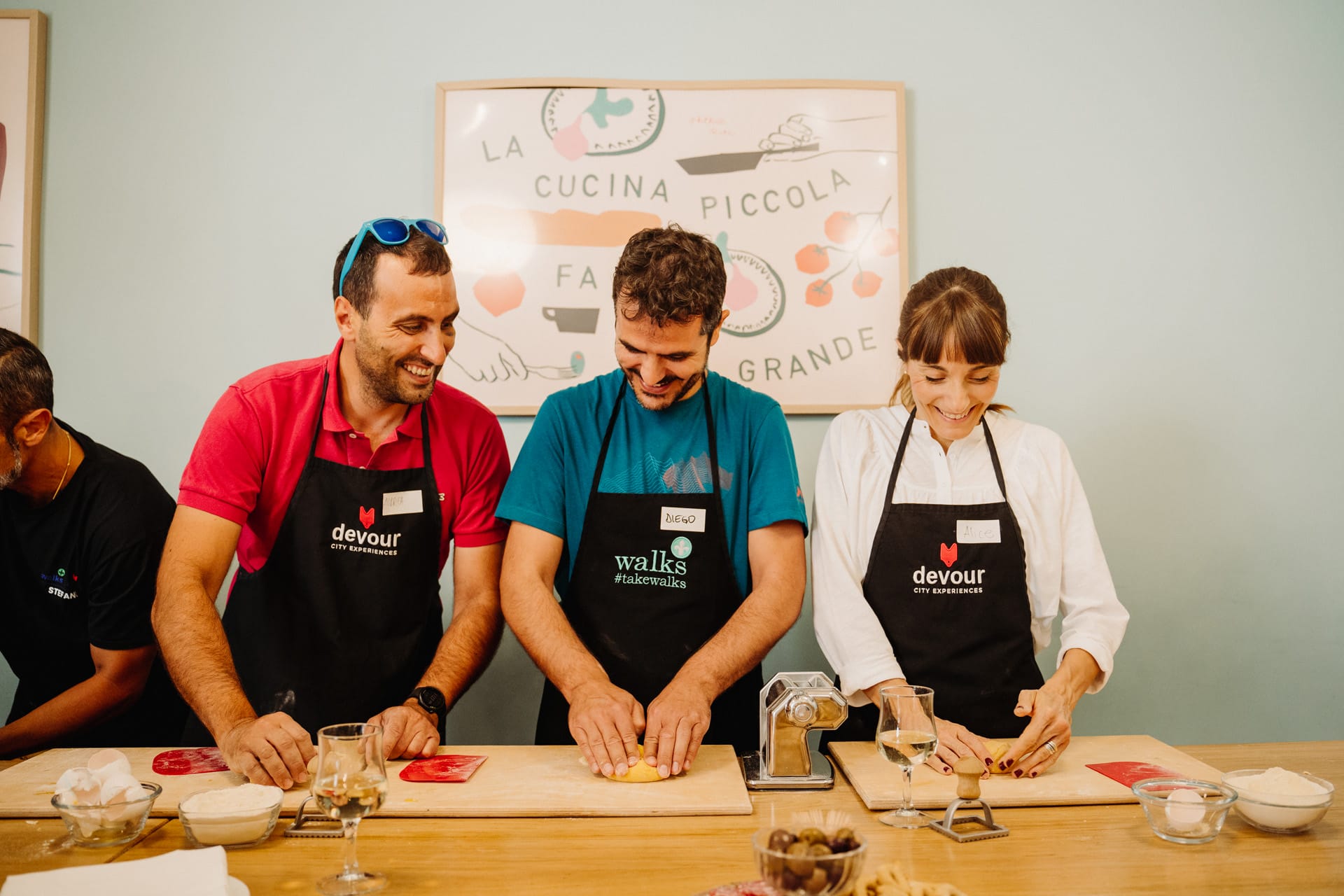 Three smiling participants kneading homemade pasta in Rome side by side during a cooking in Rome, wearing aprons from Devour and Walks of Italy.