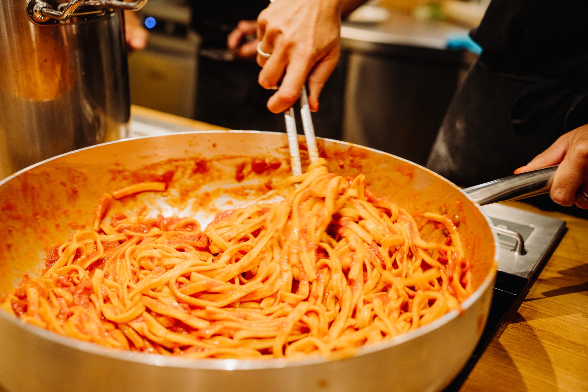 Close-up of freshly cooked pasta being stirred in a pan with rich tomato sauce during a hands-on cooking class.